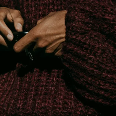 Hands wrapped around a black cup against textured burgundy knitwear.