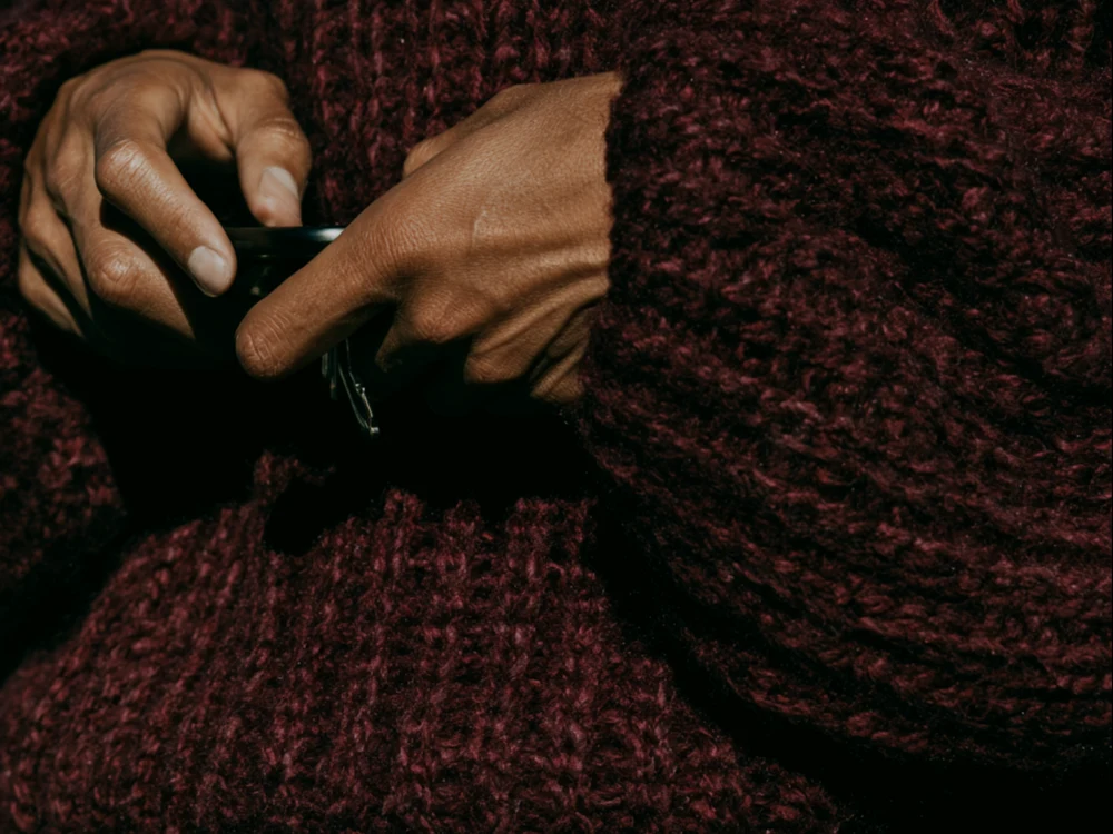 Hands wrapped around a black cup against textured burgundy knitwear.