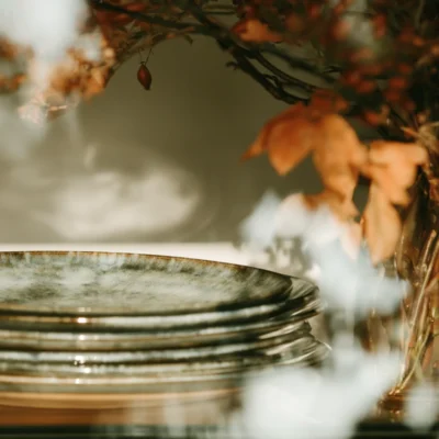 Stacked ceramic plates beneath autumn leaves and warm amber foliage, photographed with a soft editorial focus.