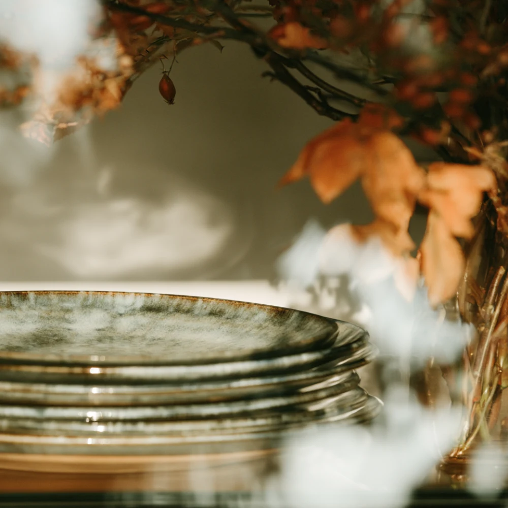 Stacked ceramic plates beneath autumn leaves and warm amber foliage, photographed with a soft editorial focus.