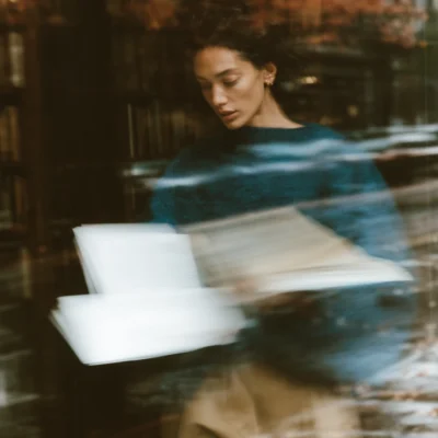 Woman in a dark teal sweater reading beside an open book in a softly blurred autumn scene. autumn editorial stock images