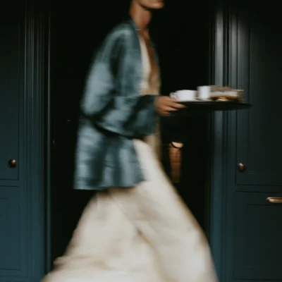 Motion-blurred figure in cream and blue carrying a tray through a dark blue interior.