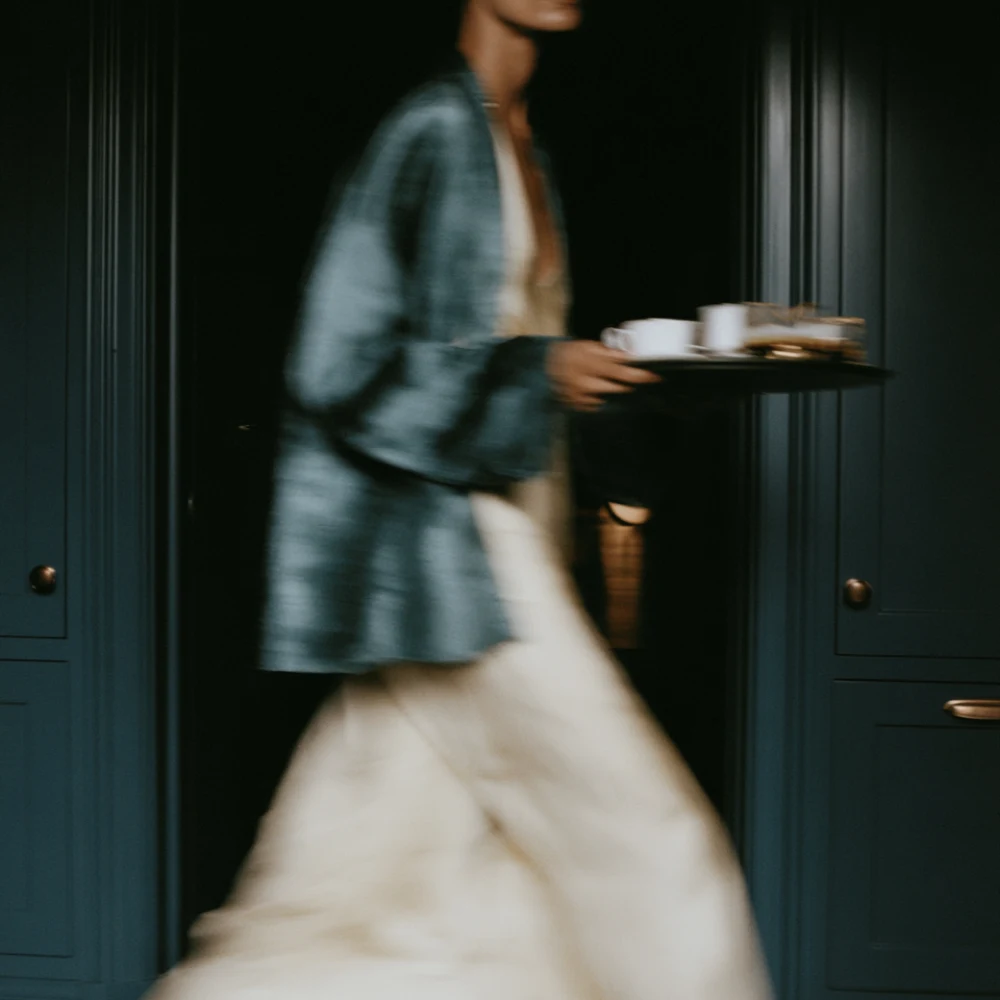 Motion-blurred figure in cream and blue carrying a tray through a dark blue interior.