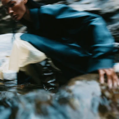 Motion-blurred model in deep blue clothing moving across wet rocks outdoors.