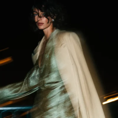 Woman in a silver dress and white evening coat against a dark background with warm light trails.