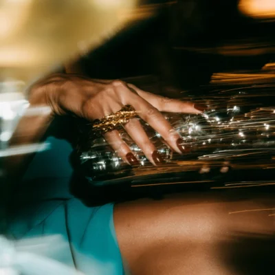 Hand with gold statement rings resting on a reflective jewelled evening bag.