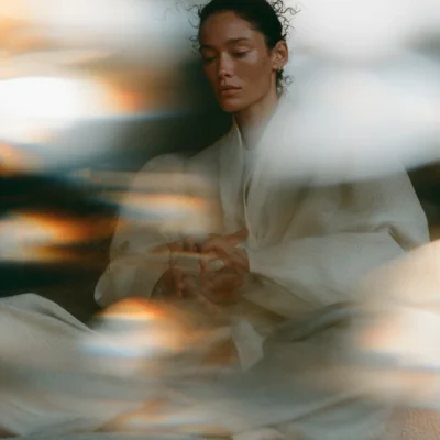 Seated woman in white surrounded by warm prismatic light for Inner Edit Volume 1.