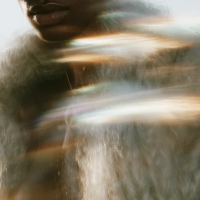 Close-up white fabric and portrait crossed by soft gold and rainbow light streaks.
