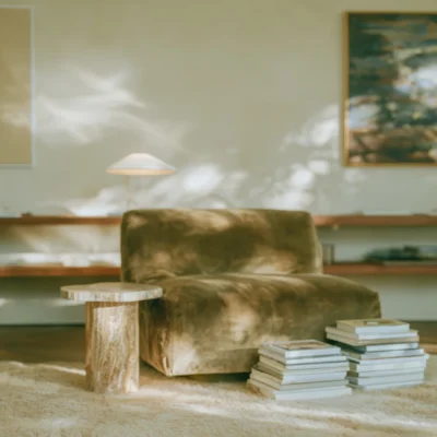 Softly lit olive armchair with stacks of books in a warm neutral interior.