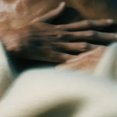 Softly blurred hands resting together against warm cream fabric.